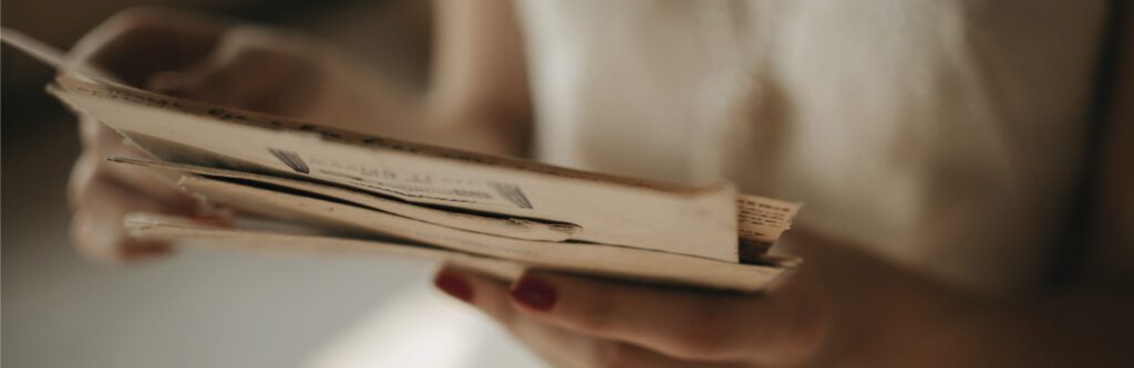 A person with red-painted nails holds and reads through a collection of old, yellowed papers and letters.