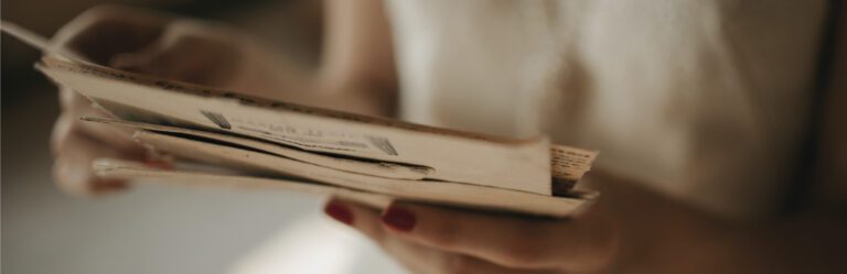 A person with red-painted nails holds and reads through a collection of old, yellowed papers and letters.