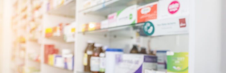 A pharmacy shelf stocked with various medicines and health products. Shelves are filled with boxes and bottles of different sizes and colors. The background is slightly blurred.