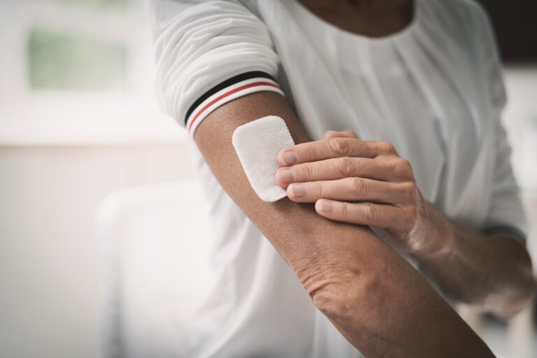A person places a large adhesive patch on their upper arm.