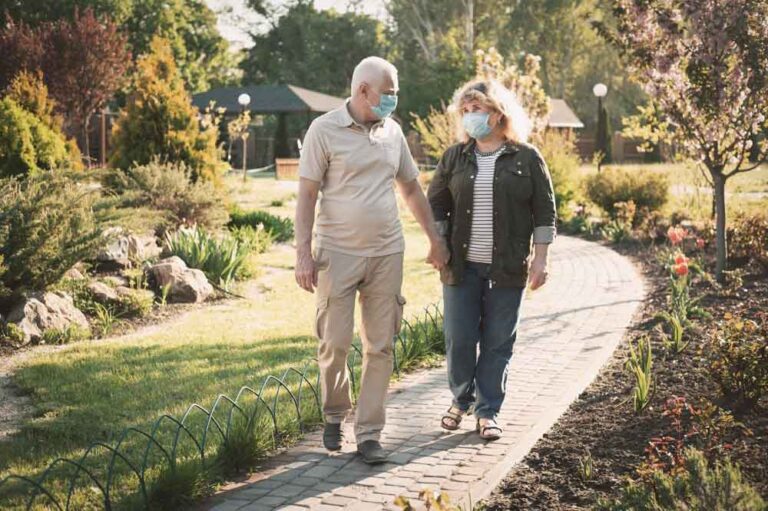 A couple walking in a park while wearing masks.