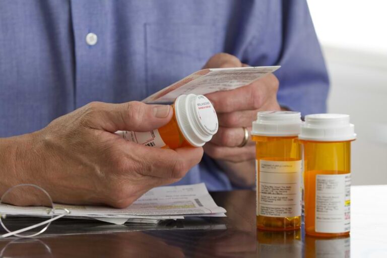 Closeup of person reading prescription information with pill bottles.