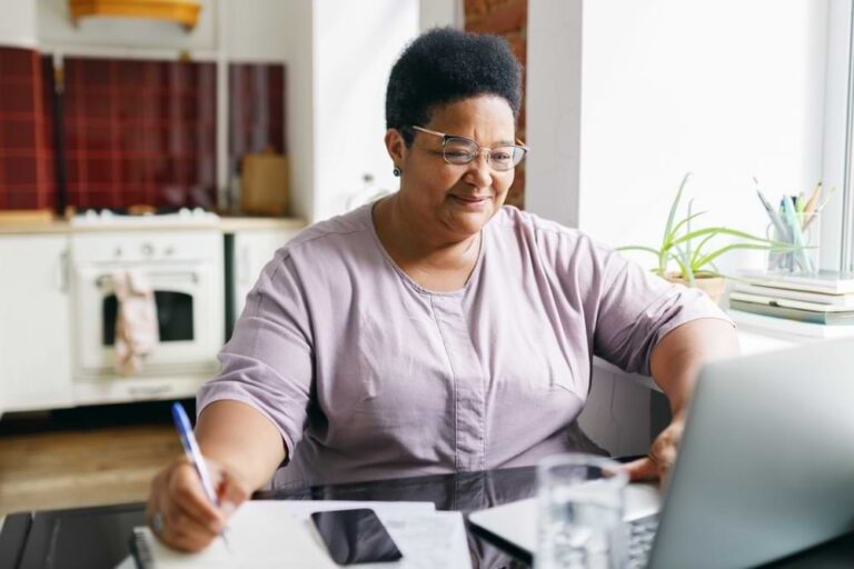 Woman sitting at laptop with a pen in hand and a calculator.