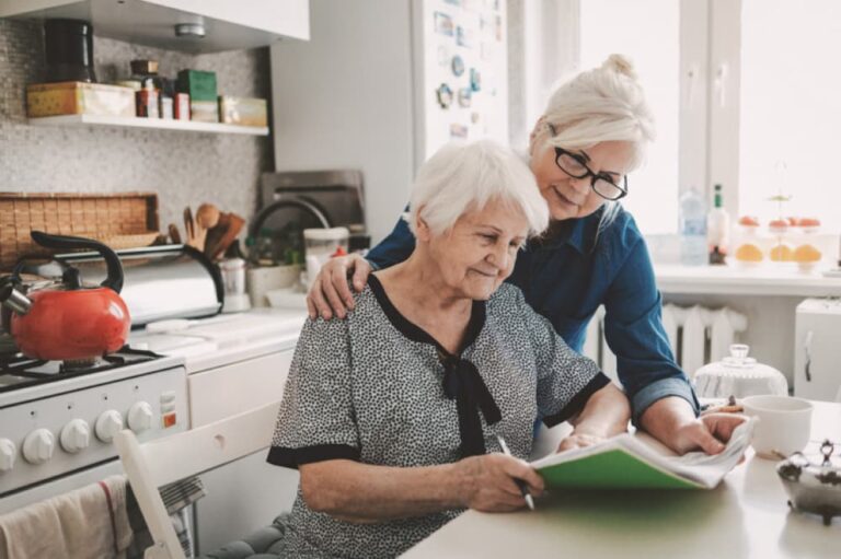 Two women looking at paperwork in a kitchen.