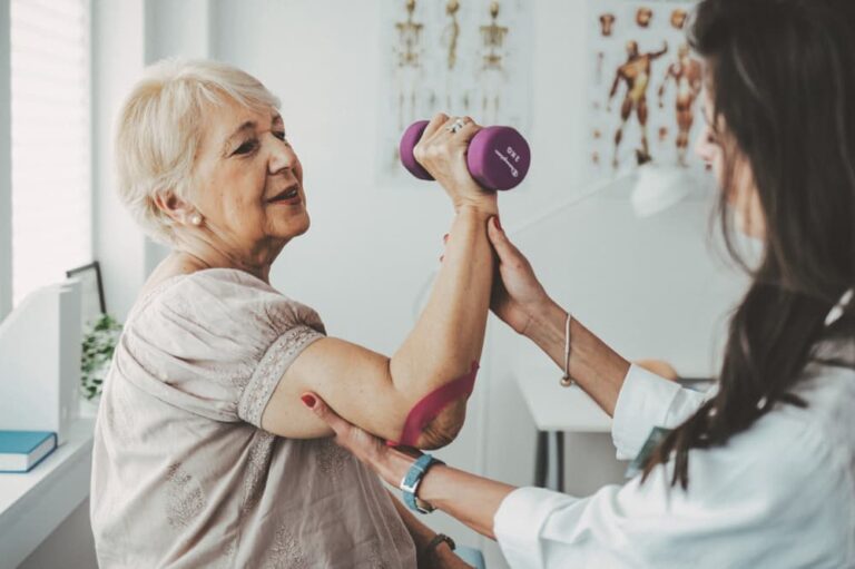 Woman at a physical therapy session, being guided to lift a barbell by her healthcare provider.